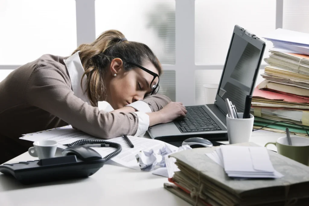 Exhausted woman asleep at her desk with head on laptop symbolizing constant fatigue and low energy