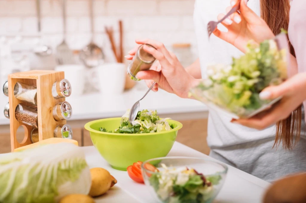 Person preparing a fresh salad with leafy greens and vegetables in a bright kitchen, representing heart-supportive nutrition and holistic cardiovascular wellness.